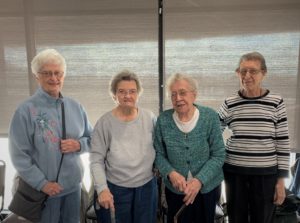 4 elderly adults standing next to eachother in front of a window